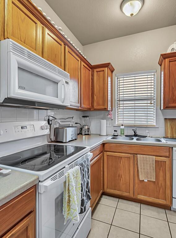 kitchen featuring white appliances, tasteful backsplash, brown cabinets, and a sink