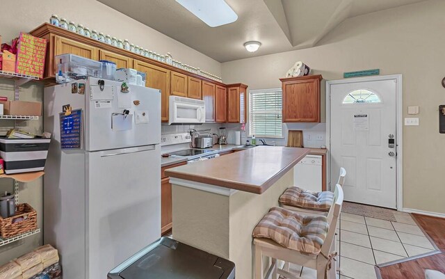 kitchen with white appliances, brown cabinetry, a kitchen island, light countertops, and a sink