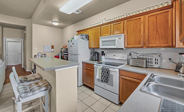 kitchen with white appliances, brown cabinetry, a kitchen breakfast bar, light countertops, and a sink