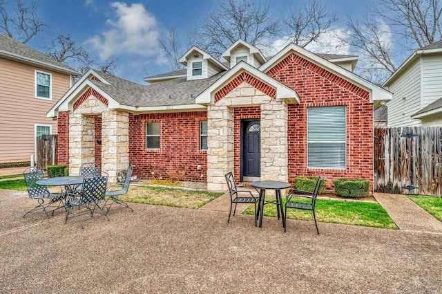 view of front of home with outdoor dining area, brick siding, a patio area, fence, and stone siding