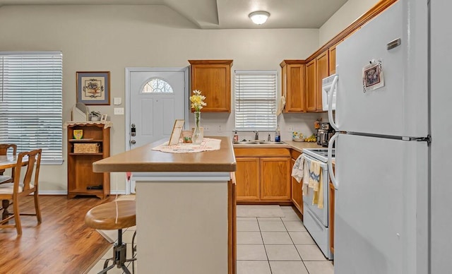 kitchen featuring white appliances, brown cabinets, a sink, and a kitchen bar