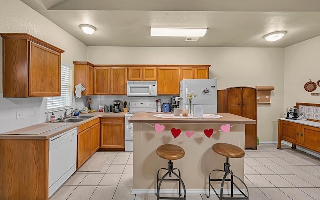 kitchen featuring light tile patterned floors, a breakfast bar area, white appliances, a sink, and backsplash