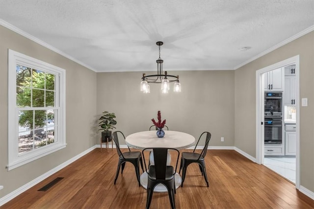 dining room with a textured ceiling, light hardwood / wood-style flooring, and ornamental molding