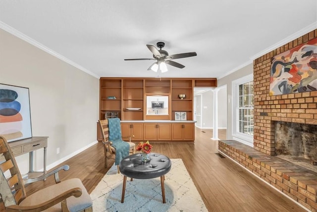 living room with light hardwood / wood-style floors, a brick fireplace, ceiling fan, and crown molding