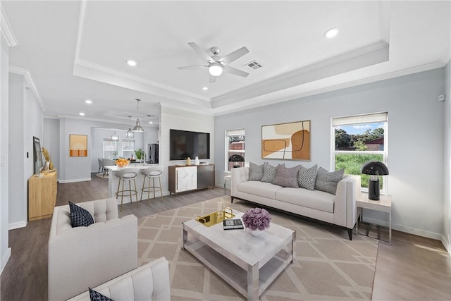 living room featuring wood-type flooring, a tray ceiling, and crown molding