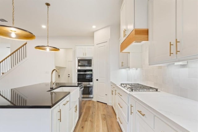 kitchen with pendant lighting, backsplash, white cabinets, appliances with stainless steel finishes, and light hardwood / wood-style floors