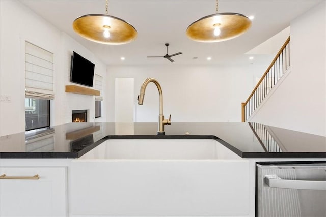 kitchen with white cabinets, dishwashing machine, a fireplace, and hanging light fixtures