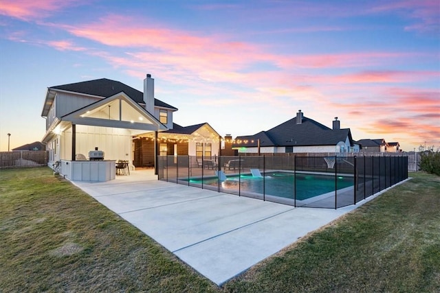 pool at dusk with area for grilling, an outdoor bar, a patio area, and a lawn