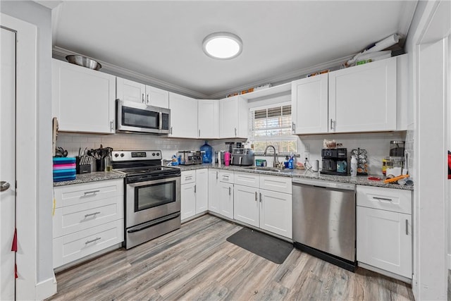 kitchen featuring sink, light stone counters, light hardwood / wood-style flooring, white cabinets, and appliances with stainless steel finishes