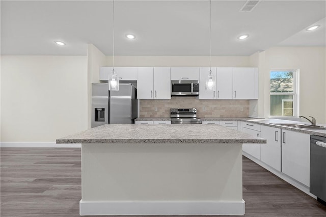 kitchen with white cabinets, decorative light fixtures, a kitchen island, and stainless steel appliances