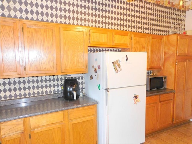 kitchen with white fridge, light tile patterned floors, and tasteful backsplash