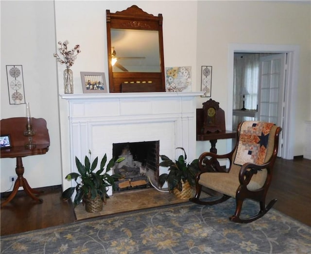 sitting room featuring ceiling fan, dark wood-type flooring, and a brick fireplace