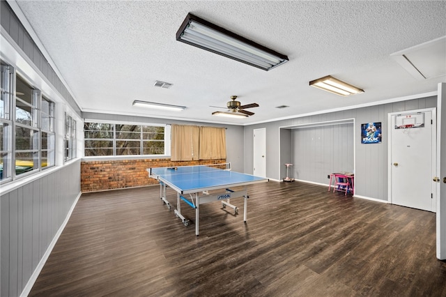 game room with dark hardwood / wood-style floors, ceiling fan, ornamental molding, a textured ceiling, and brick wall