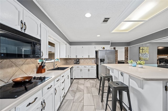 kitchen featuring black appliances, white cabinets, sink, tasteful backsplash, and a breakfast bar area