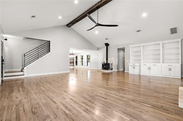 unfurnished living room with beamed ceiling, light hardwood / wood-style floors, a wood stove, and ceiling fan