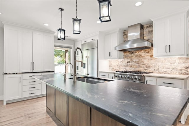 kitchen featuring wall chimney exhaust hood, white cabinetry, stainless steel appliances, and a kitchen island with sink