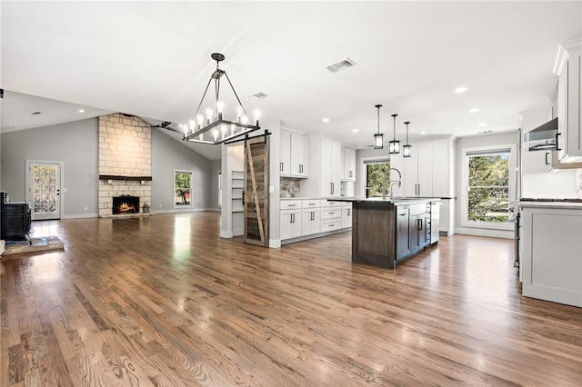 kitchen with pendant lighting, lofted ceiling, a center island with sink, light hardwood / wood-style floors, and white cabinetry