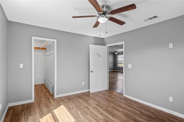 unfurnished bedroom featuring a walk in closet, a closet, ceiling fan, and light hardwood / wood-style floors