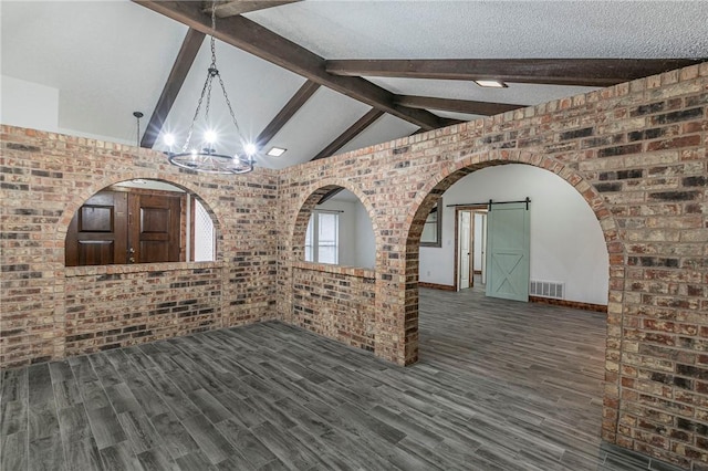 interior space featuring brick wall, a barn door, dark wood-type flooring, and vaulted ceiling with beams