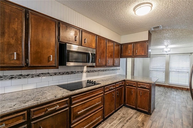 kitchen featuring a textured ceiling, light hardwood / wood-style flooring, black electric cooktop, kitchen peninsula, and backsplash