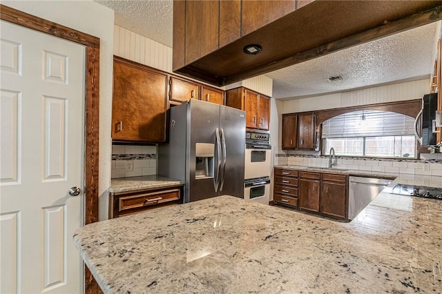 kitchen with sink, appliances with stainless steel finishes, light stone counters, a textured ceiling, and kitchen peninsula