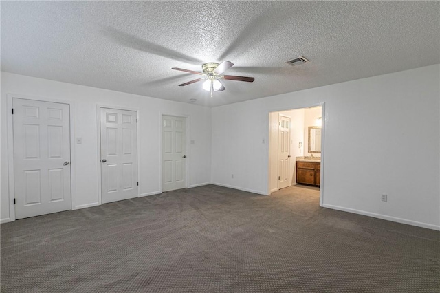 unfurnished bedroom featuring ceiling fan, connected bathroom, a textured ceiling, dark carpet, and two closets