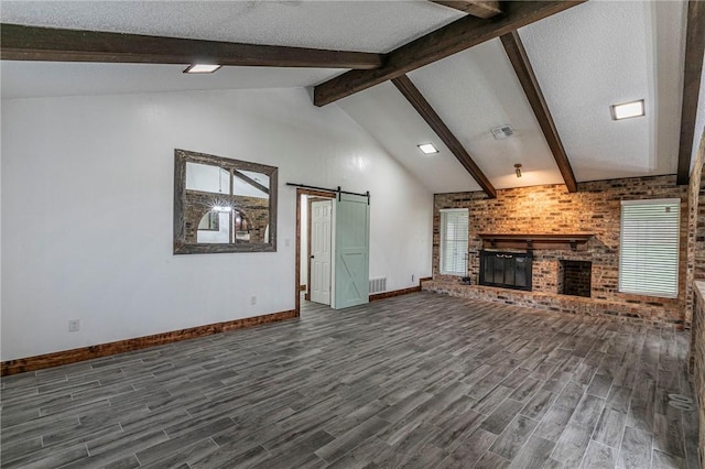 unfurnished living room featuring a barn door, a textured ceiling, dark hardwood / wood-style floors, beamed ceiling, and a fireplace