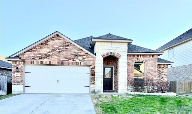 french country style house with a garage, driveway, roof with shingles, and brick siding