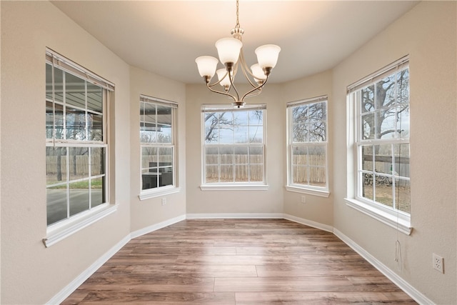 unfurnished dining area featuring plenty of natural light, wood finished floors, baseboards, and a chandelier