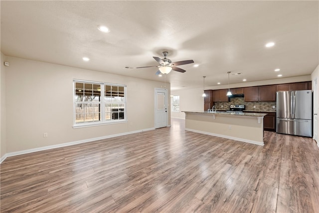 kitchen featuring ceiling fan, stainless steel appliances, open floor plan, light wood-style floors, and tasteful backsplash