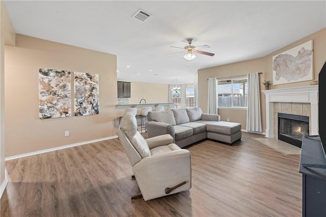 living room featuring ceiling fan, a tile fireplace, and light wood-type flooring