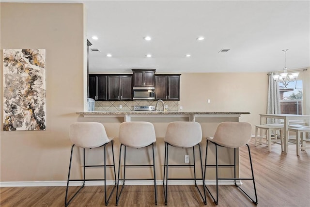 kitchen featuring a breakfast bar area, dark brown cabinets, appliances with stainless steel finishes, light hardwood / wood-style floors, and decorative backsplash