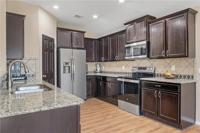 kitchen featuring lofted ceiling, sink, appliances with stainless steel finishes, dark brown cabinets, and light hardwood / wood-style floors