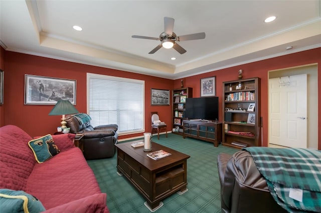 carpeted living room with a raised ceiling, ceiling fan, and crown molding