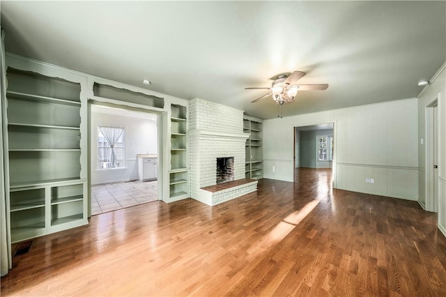 unfurnished living room with built in features, hardwood / wood-style flooring, a brick fireplace, and ceiling fan