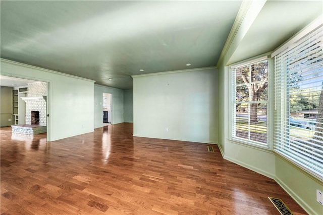 unfurnished room featuring hardwood / wood-style flooring, a brick fireplace, and ornamental molding