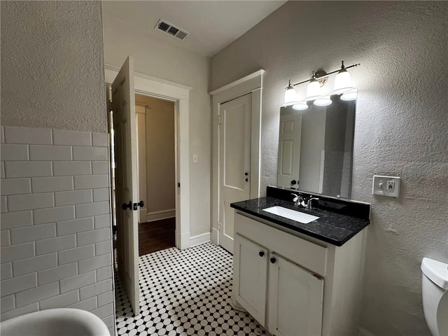 bathroom with tile patterned flooring, vanity, toilet, and tile walls