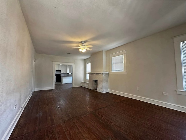 unfurnished living room featuring dark hardwood / wood-style floors, a brick fireplace, and ceiling fan