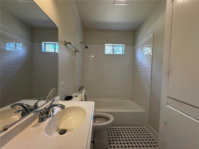 full bathroom with a textured ceiling, tiled shower / bath combo, toilet, and sink