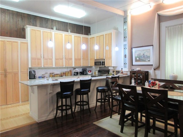 kitchen featuring kitchen peninsula, black stove, decorative light fixtures, dark hardwood / wood-style floors, and a breakfast bar area