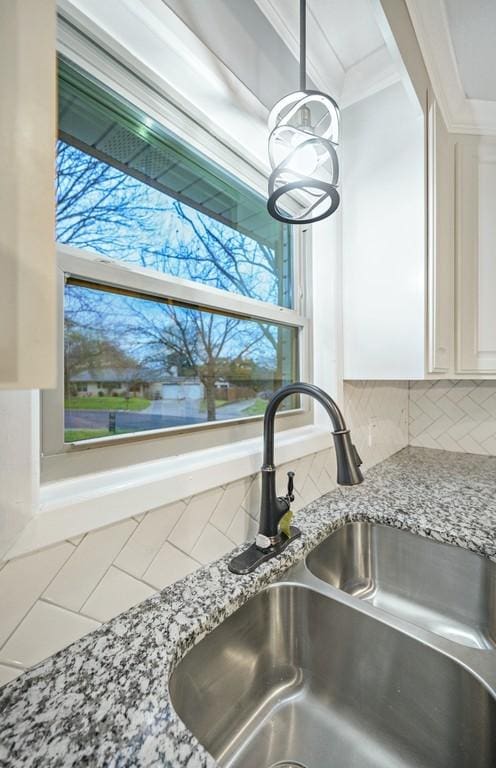 details featuring backsplash, white cabinets, sink, ornamental molding, and light stone counters