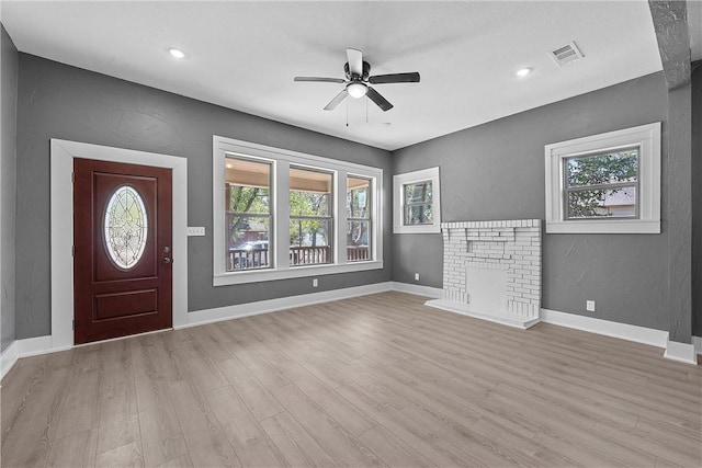 entryway featuring ceiling fan, light wood-type flooring, a wealth of natural light, and a brick fireplace