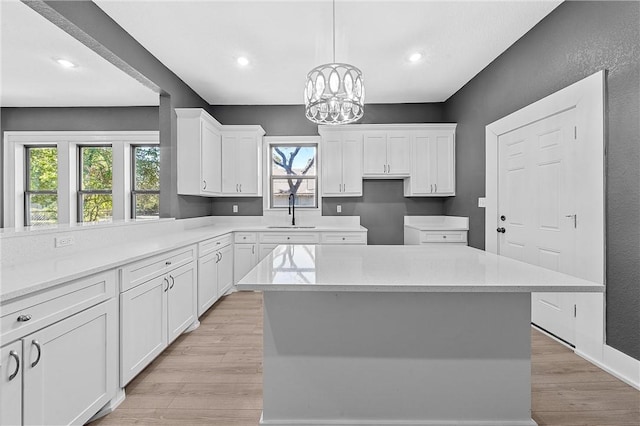 kitchen featuring white cabinetry, sink, an inviting chandelier, a kitchen island, and light wood-type flooring