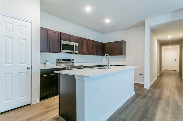 kitchen featuring a sink, light countertops, appliances with stainless steel finishes, dark brown cabinets, and an island with sink