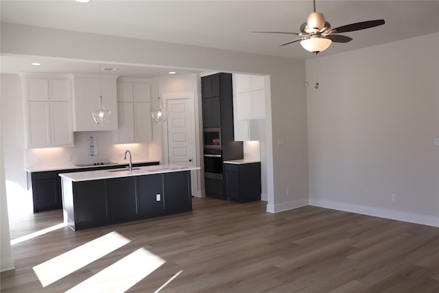 kitchen with white cabinetry, a center island with sink, dark hardwood / wood-style flooring, decorative backsplash, and oven