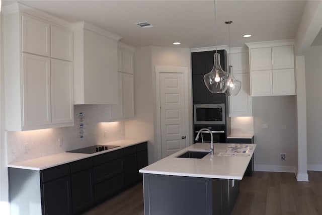 kitchen featuring sink, a center island with sink, pendant lighting, decorative backsplash, and black appliances