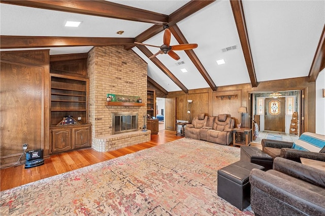 living room featuring light wood-type flooring, a brick fireplace, ceiling fan, wooden walls, and lofted ceiling with beams