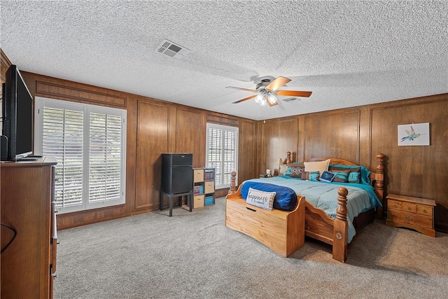 bedroom featuring a textured ceiling, ceiling fan, light carpet, and wooden walls