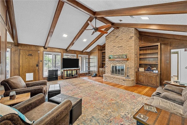 living room with light wood-type flooring, a textured ceiling, lofted ceiling with beams, a fireplace, and wood walls