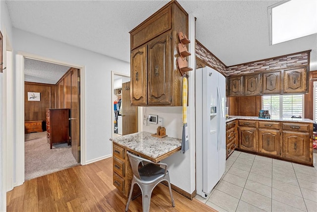 kitchen with light stone counters, a textured ceiling, light hardwood / wood-style flooring, white fridge with ice dispenser, and wood walls